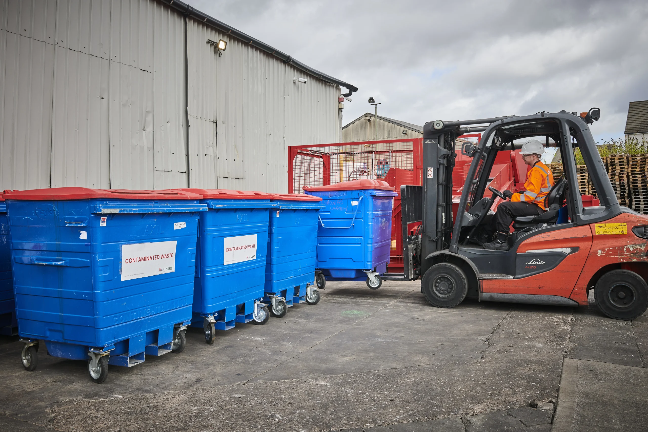 Forklift driver moving a hazardous waste bin. Four bins showing contaminated waste