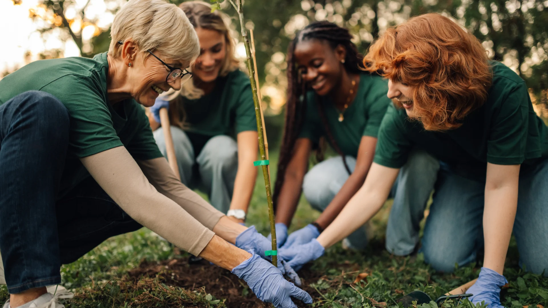 Happy and cheerful volunteers wearing green t shirts are planting a young tree in the forest, working together to protect the environment